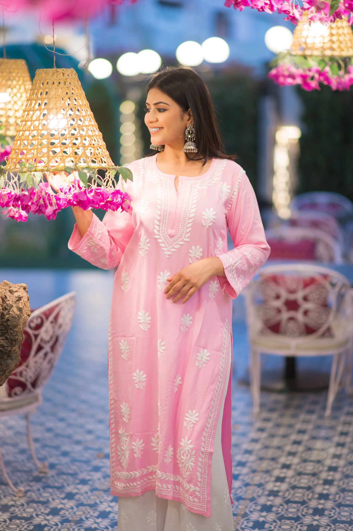 Side view of a woman gracefully posing in a stylish pink Lucknow Chikan kurta featuring exquisite white traditional embroidery.