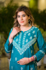 In a close-up front view, a woman touching her hair wears a teal blue kurta with white floral and geometric embroidery.