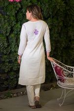 Back full shot of a woman in a white mulmul fabric kurta and pants with purple embroidery.