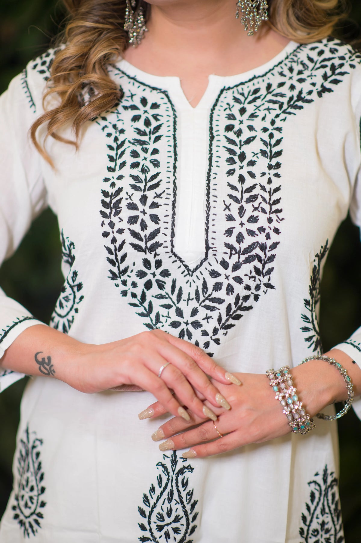 Close-up front view of the black intricate embroidery on a white chikankari fabric kurta's neckline.