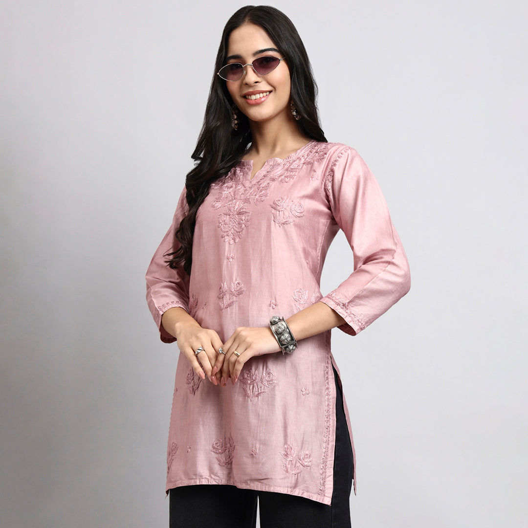 Woman wearing a pink embroidered top on a gray background