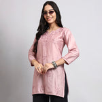 Woman wearing a pink embroidered top on a gray background