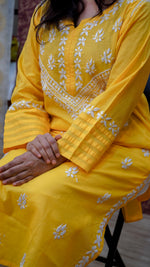 Woman sitting and wearing a yellow cotton kurti with white Chikankari work, showing embroidery on sleeves and front clearly.