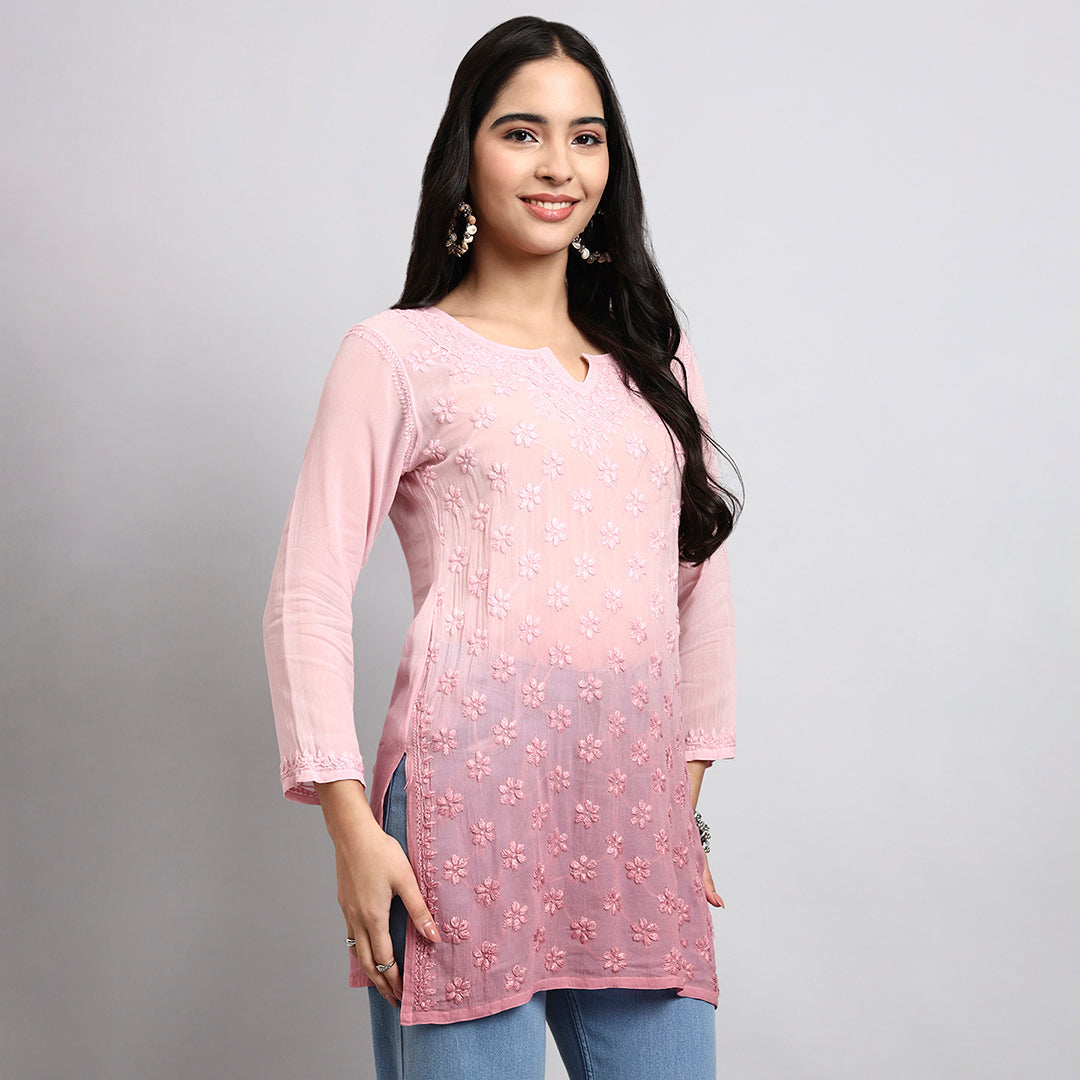 Woman wearing a pink embroidered short kurta with a plain background