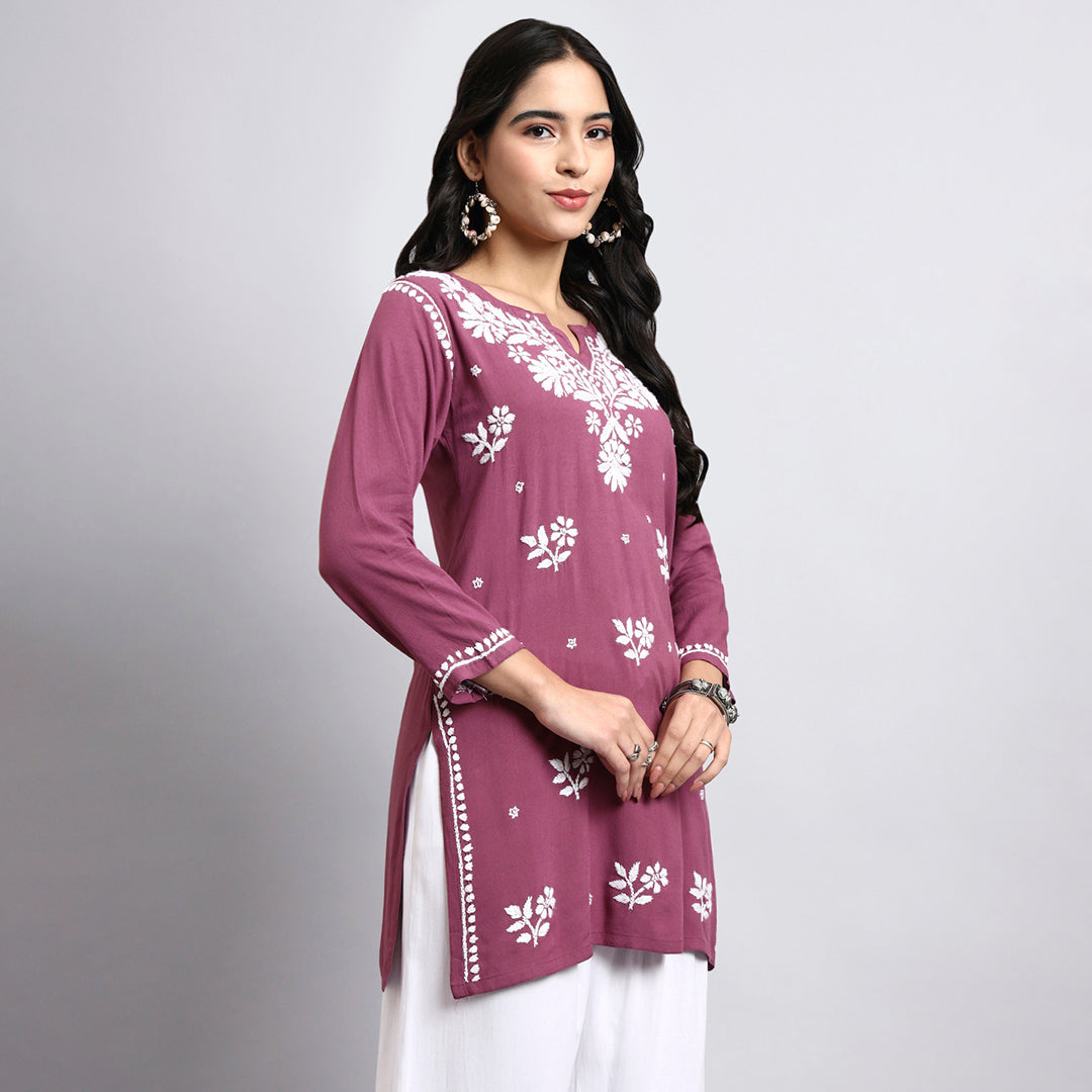 Woman wearing a purple embroidered top with white patterns on a gray background