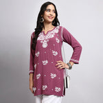 Woman wearing a purple embroidered kurta with white pants on a gray background