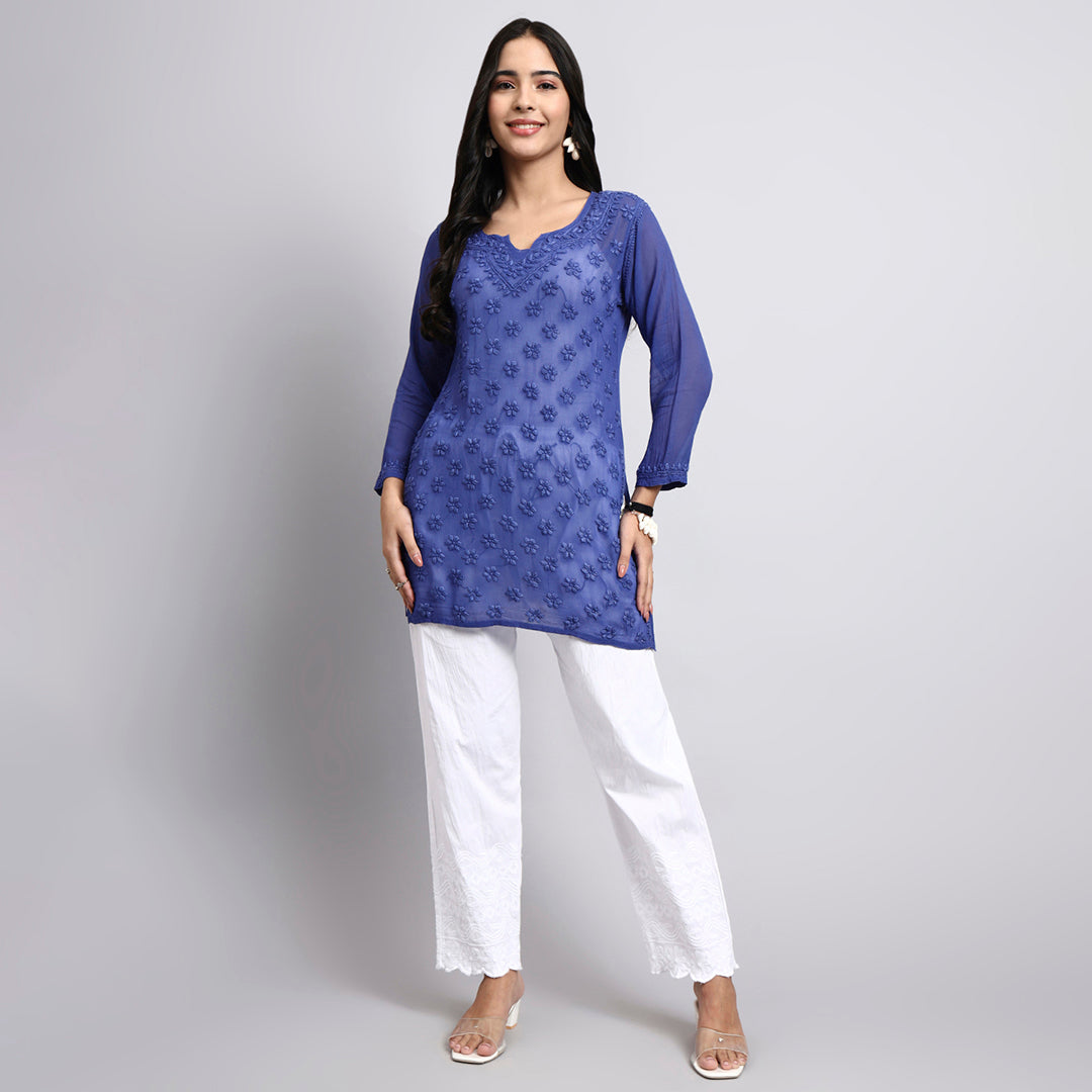 Woman wearing a blue patterned top and white pants on a gray background