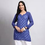 Woman wearing a blue embroidered kurta with white pants on a gray background