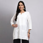 Woman wearing a white floral blouse against a gray background