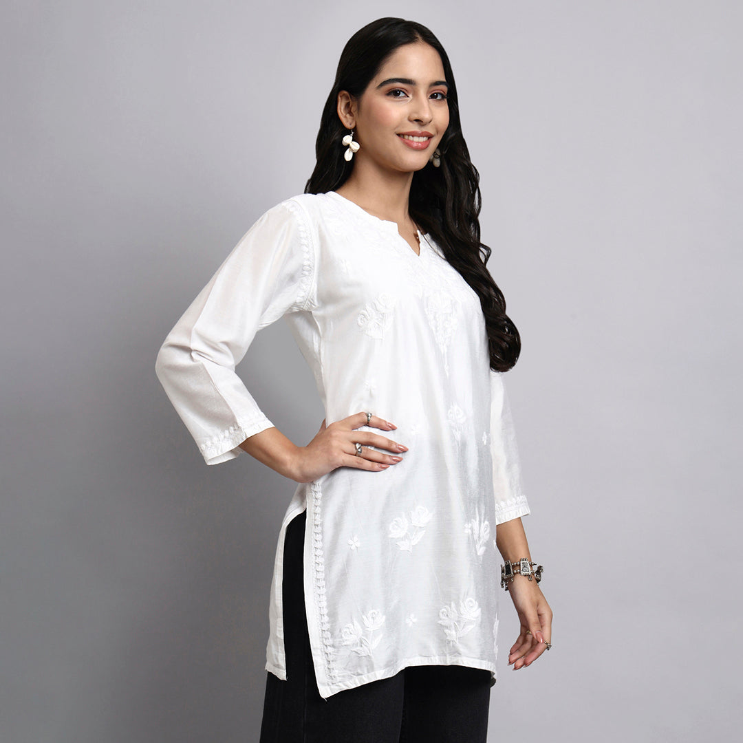 Woman wearing a white short kurta with floral patterns on a gray background