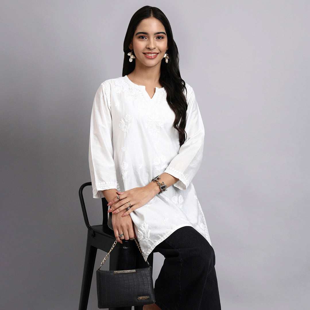 Woman in a white kurta sitting on a black stool against a gray background