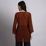 Back View Of Woman wearing a brown long-sleeve top with a subtle design on a gray background