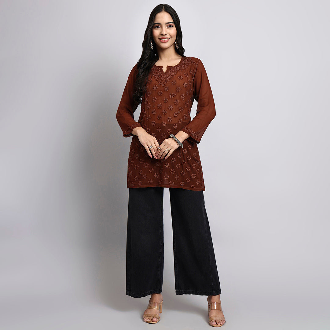 Woman wearing a brown patterned top and black pants on a gray background