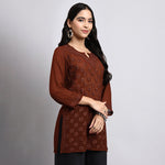 Woman wearing a brown embroidered top against a gray background