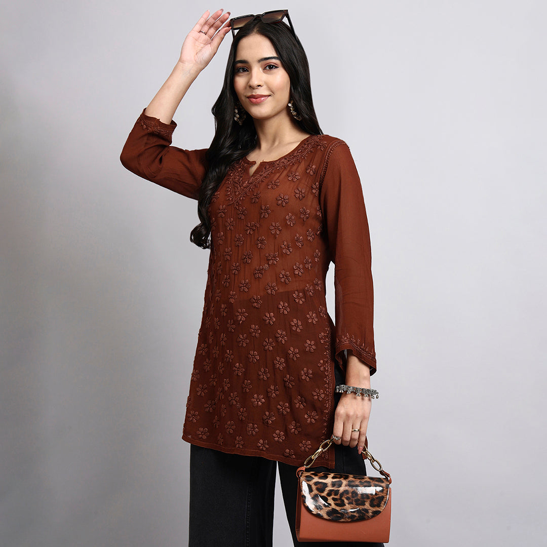 Woman wearing a brown floral top and holding a leopard print handbag against a gray background.