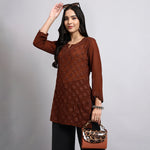 Woman wearing a brown floral top and holding a leopard print handbag against a gray background.