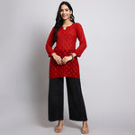 Woman wearing a red embroidered top and black pants on a gray background