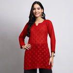 Woman wearing a red embroidered kurta against a gray background