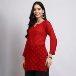 Woman wearing a red lace top against a gray background