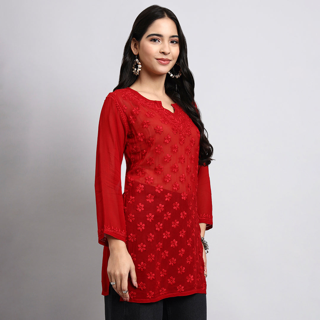 Woman wearing a red embroidered top against a gray background