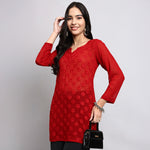 Woman wearing a red floral dress holding a black handbag against a gray background