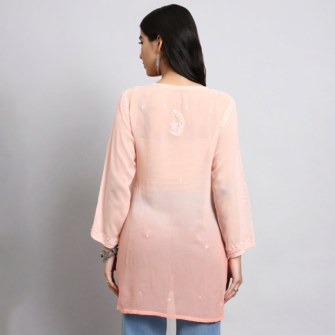 Woman wearing a light pink embroidered kurta against a gray background