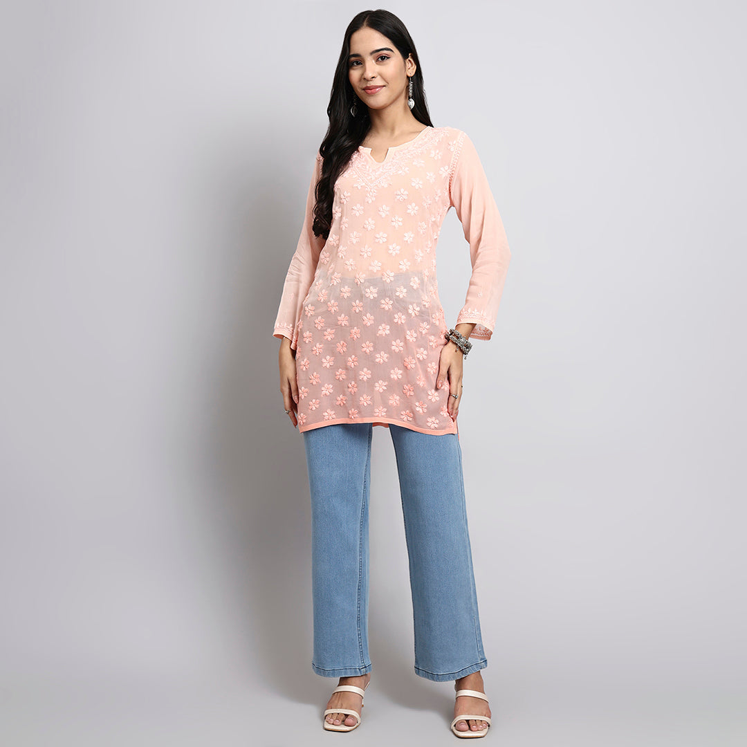 Woman wearing a peach floral short kurta and blue jeans on a gray background