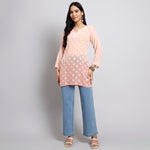 Woman wearing a peach floral short kurta and blue jeans on a gray background