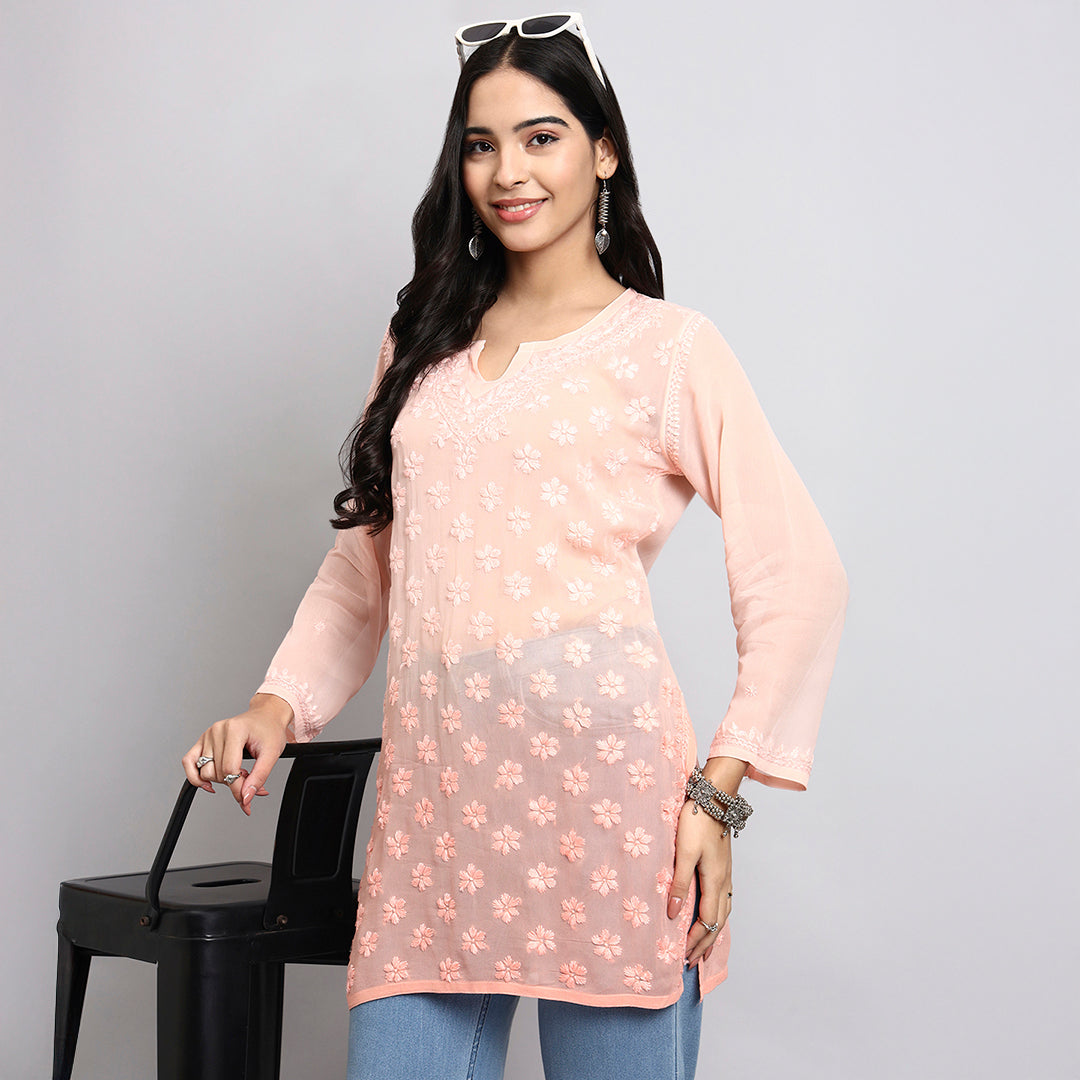 Woman wearing a light pink floral kurta with blue jeans against a gray background