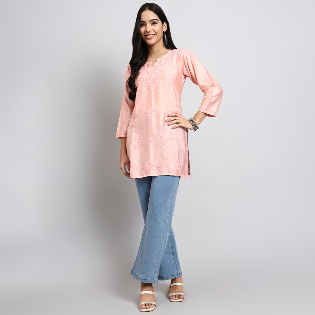 Woman wearing a pink short kurta and blue jeans on a plain background