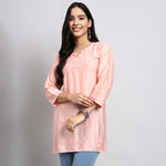 Woman wearing a pink kurta with floral patterns on a gray background