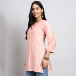 Woman wearing a light pink embroidered kurta against a plain background