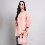 Woman wearing a pink kurta with sunglasses and a handbag on a gray background