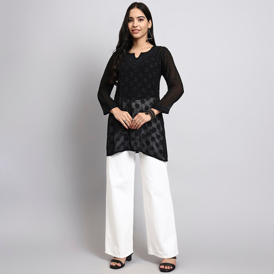 Woman wearing a black patterned short kurta with white pants on a gray background