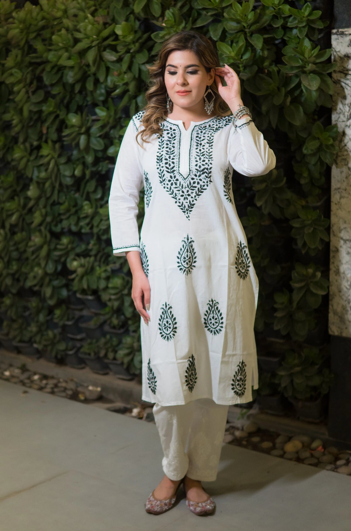 Front view of a woman in a white long mulmulkurti that has green floral embroidery on the neckline and body.