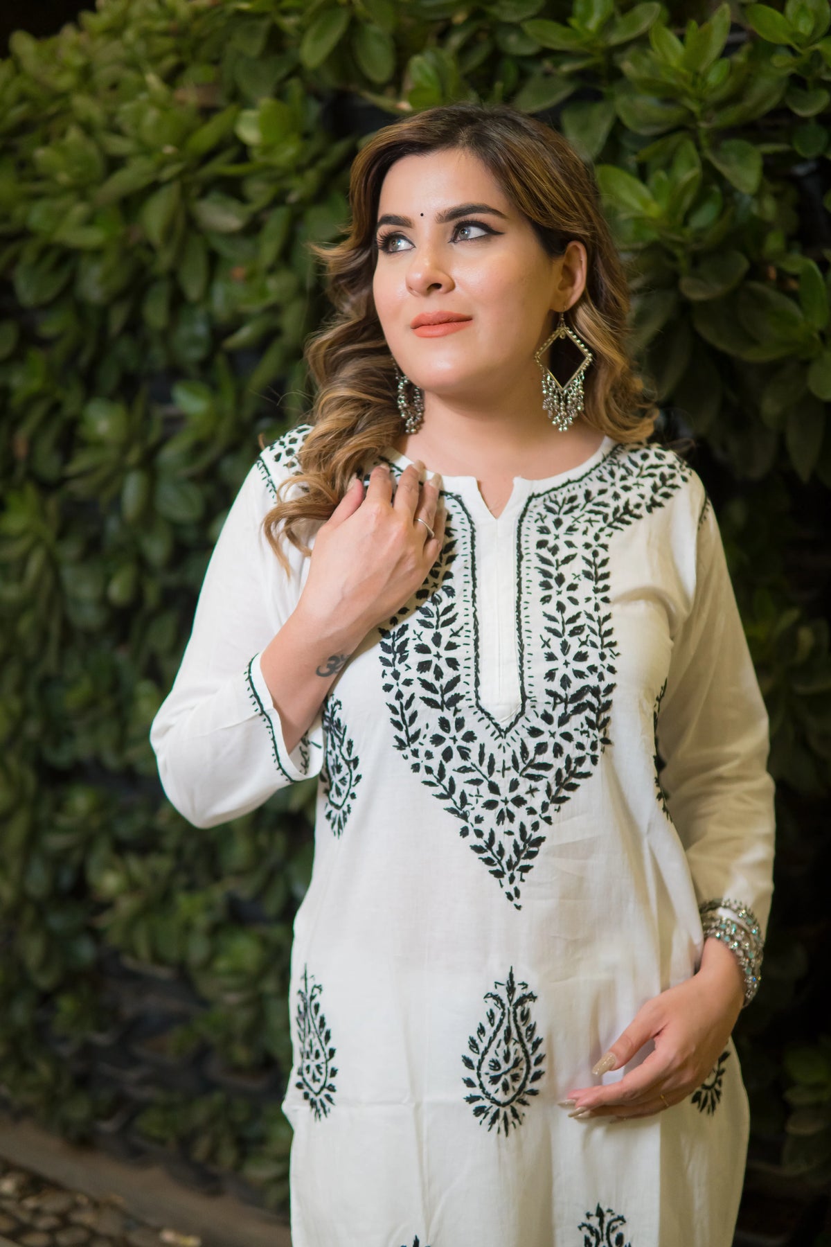 An angled view shows a woman in a white kurti that features intricate green threadwork embroidery.