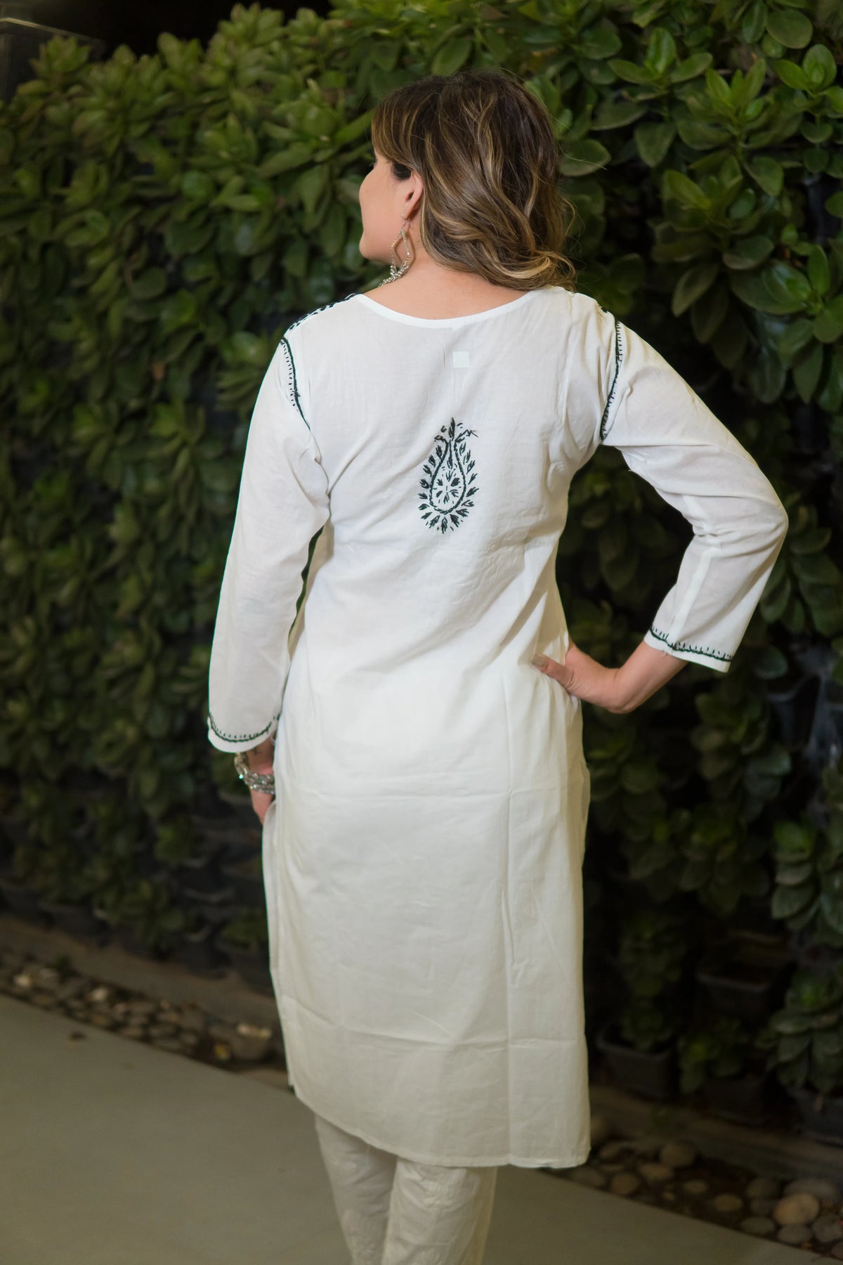 A back view of a woman shows the green detailed embroidery on the cuffs and a motif on the white mulmul kurti.