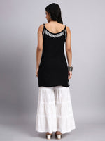 Back view of Woman wearing a black sleeveless top with white embroidery and white checkered pants on a gray background