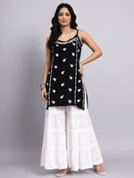 Woman wearing a black sleeveless chikankari kurti with white patterns and white sharara on a gray background
