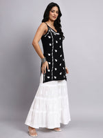 Woman wearing a black top with white patterns and a white skirt on a gray background
