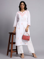 Full view of Woman wearing a white embroidered kurta with white pants, holding a red handbag on a gray background.