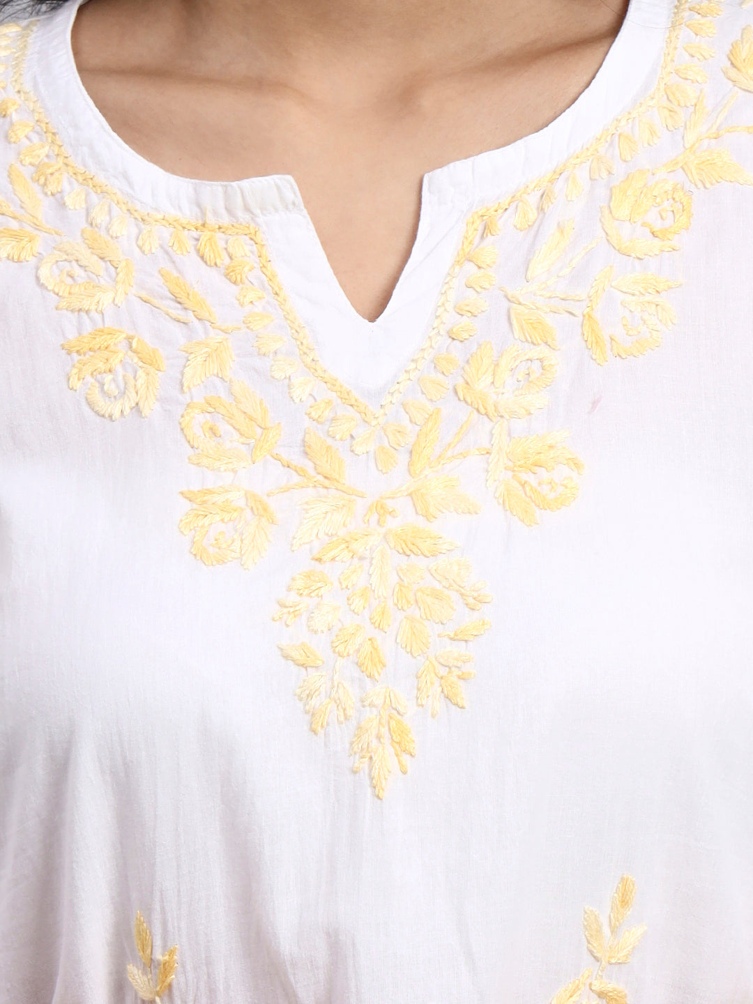 Close up of White garment with yellow floral embroidery on a plain background
