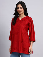 Woman wearing a red embroidered kurti against a gray background