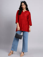 Full view of Woman wearing a red top and blue jeans holding a black handbag on a gray background