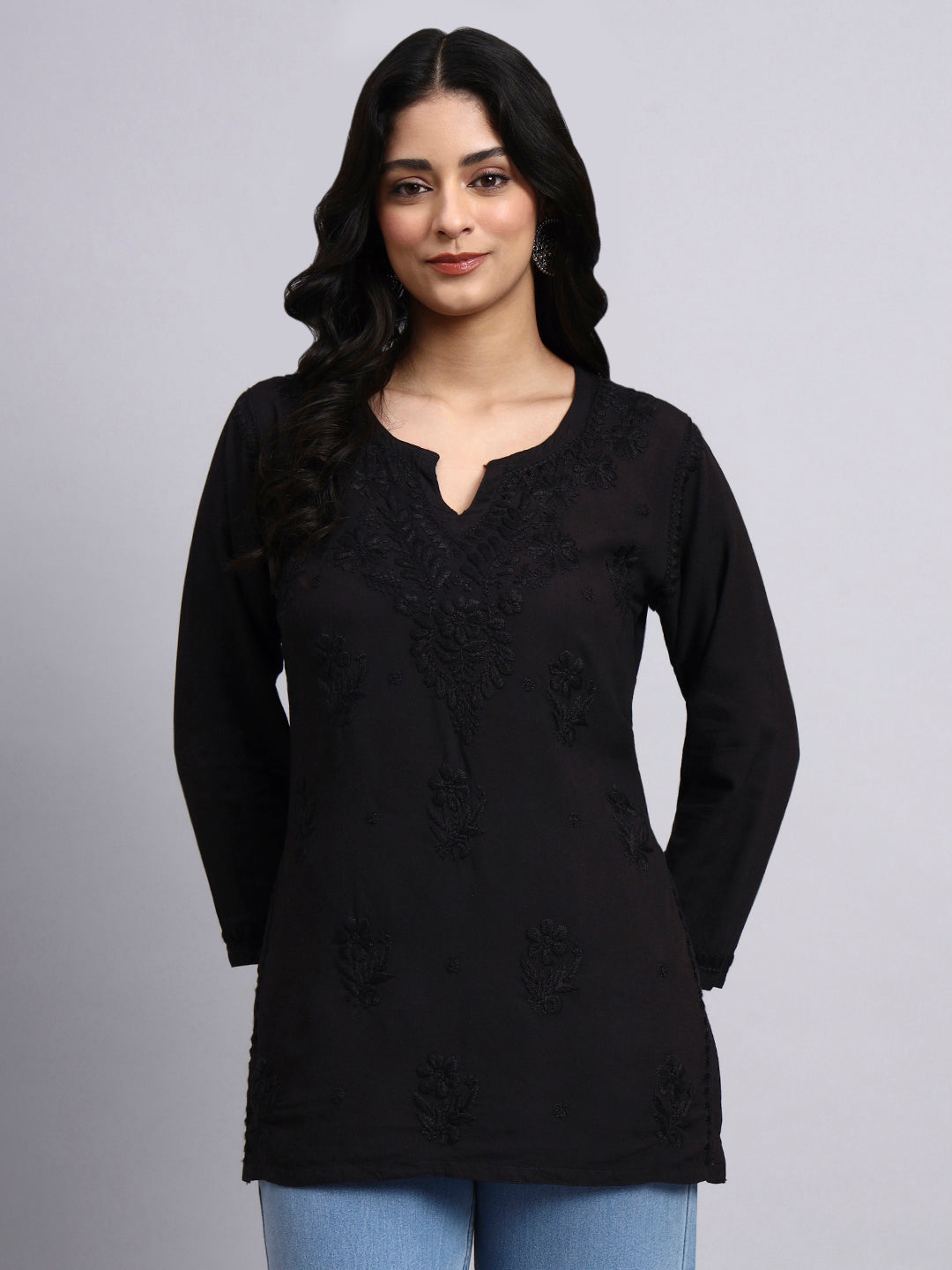 Woman wearing a black long-sleeve short kurti with floral patterns on a gray background