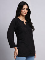Side view of Woman wearing a black long-sleeve chikankari kurti with floral embellishments on a gray background