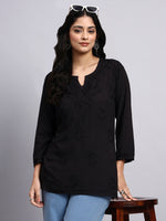Woman wearing a black embroidered top with blue jeans on a gray background