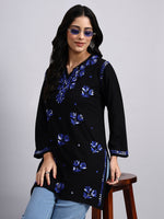 Woman wearing a black short kurta with blue floral patterns on a gray background