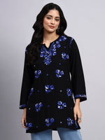 Front view of Woman wearing a black chikankari short kurti with blue floral embroidery on a gray background