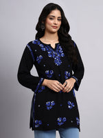 Woman wearing a black embroidered top with blue floral patterns on a gray background